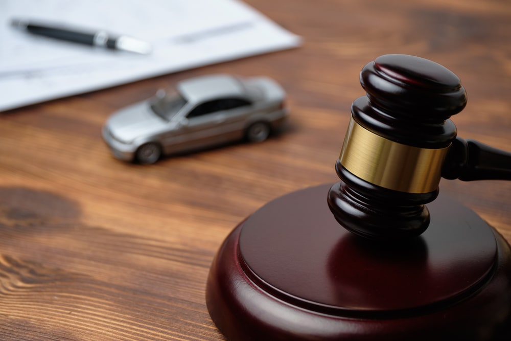 A judge’s gavel beside a small toy car and legal documents on a wooden desk symbolizes traffic court decisions.