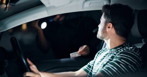 Driver pulled over at night by a police officer shining a flashlight and checking the driver’s license.