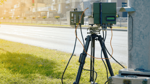A roadside speed radar camera is set up on a tripod to detect speeding vehicles