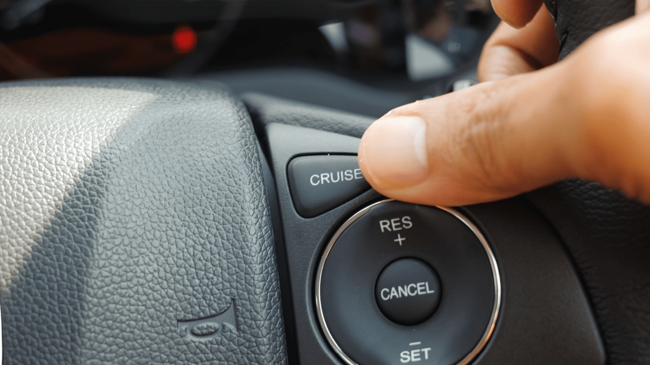 Finger pressing cruise control button on car steering wheel