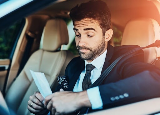 Man in suit looking at speeding ticket inside his car – how to negotiate a speeding ticket