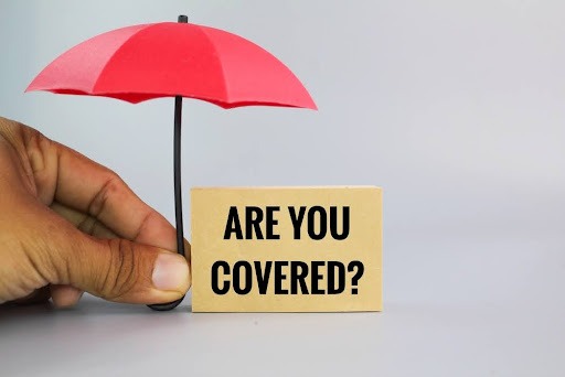 Hand holding umbrella over sign reading “Are You Covered?” – will insurance cover an accident if your license is suspended
