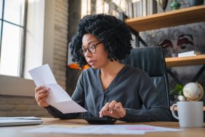 A woman is reviewing a document and using a calculator at her desk.