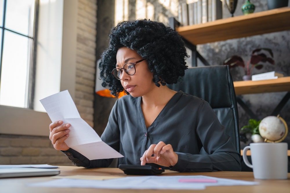 A woman is reviewing a document and using a calculator at her desk.