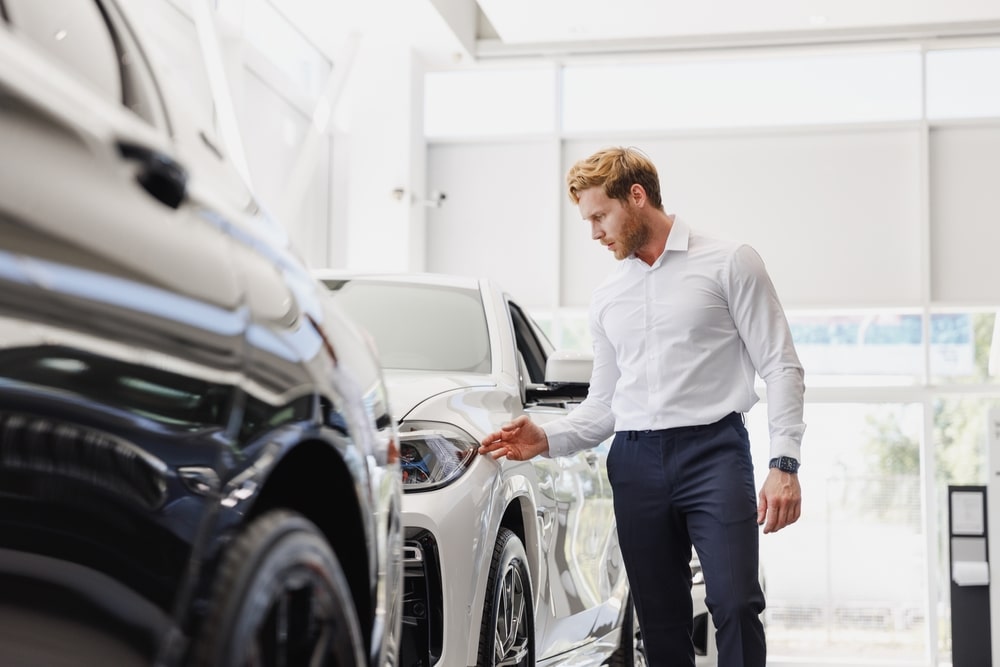 Man is inspecting a white car in a dealership showroom.