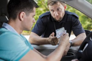 Police officer examining a driver’s license during a traffic stop in daylight, viewed through the car window.