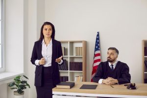 Female attorney speaks in court while a judge listens at the bench with an American flag in the background.