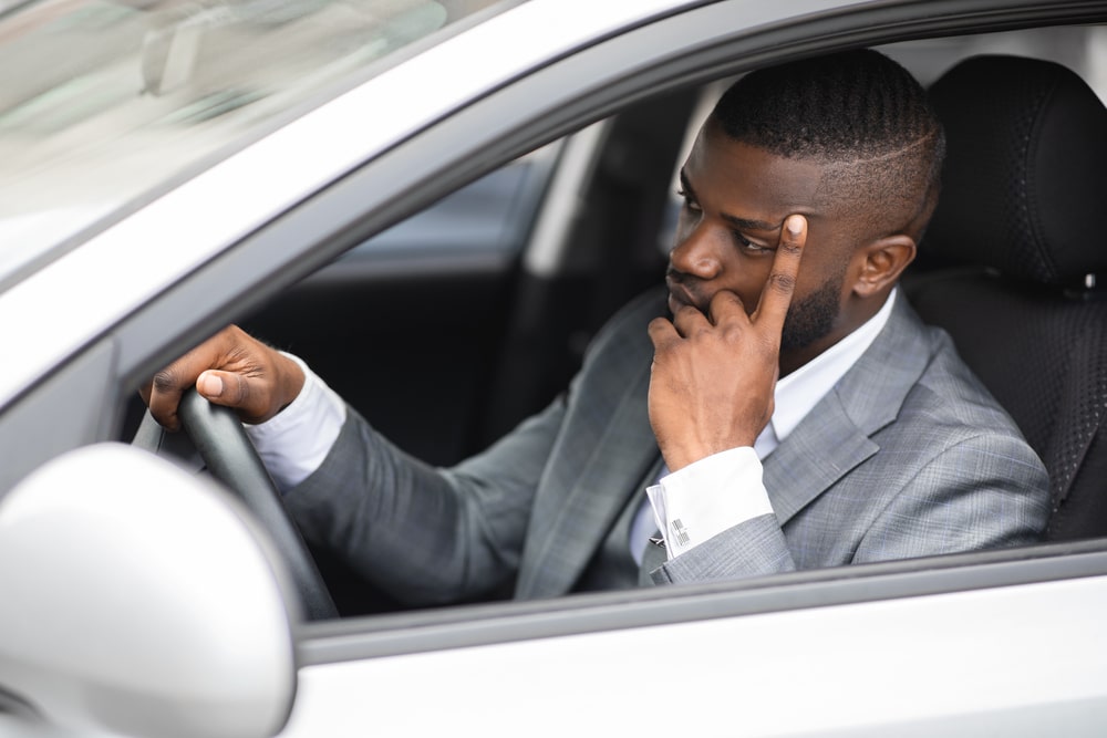 Thoughtful man in a suit sitting in his car with hand on head, appearing concerned.