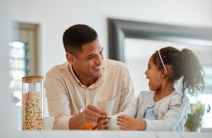 Father smiles at his daughter while eating breakfast together at home.