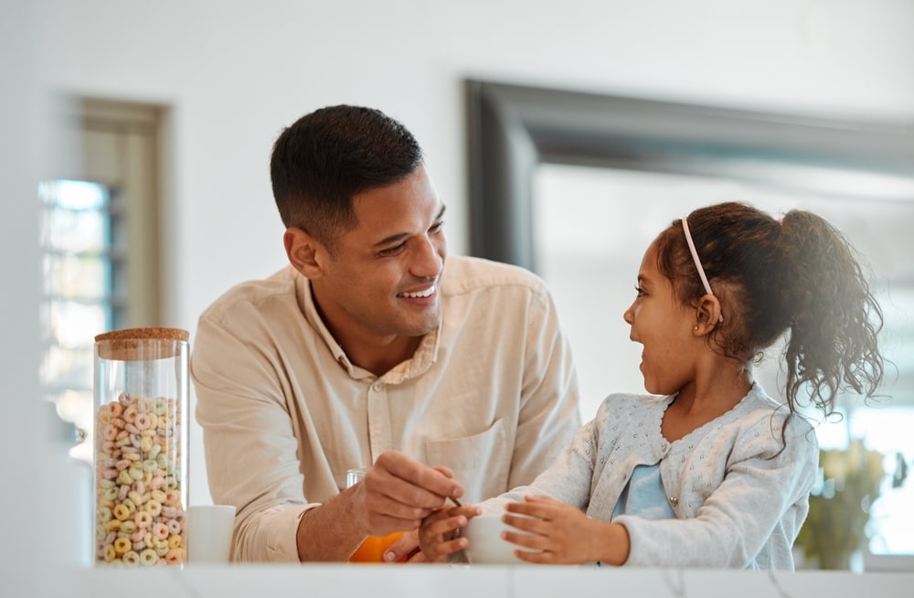 Father smiles at his daughter while eating breakfast together at home.