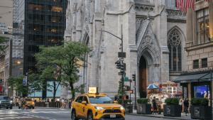 A yellow taxi is driving through a New York City street near St. Patrick’s Cathedral.