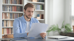 Man reviewing paperwork at a desk in a home office setting.