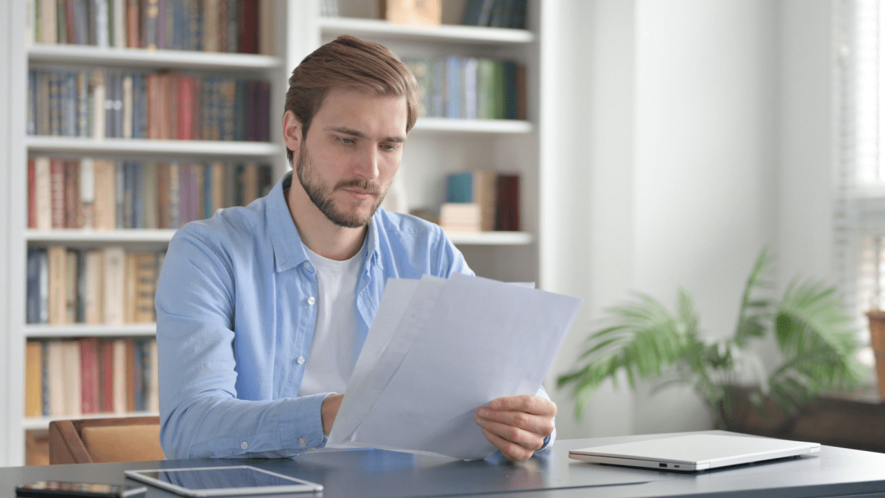 Man reviewing paperwork at a desk in a home office setting.