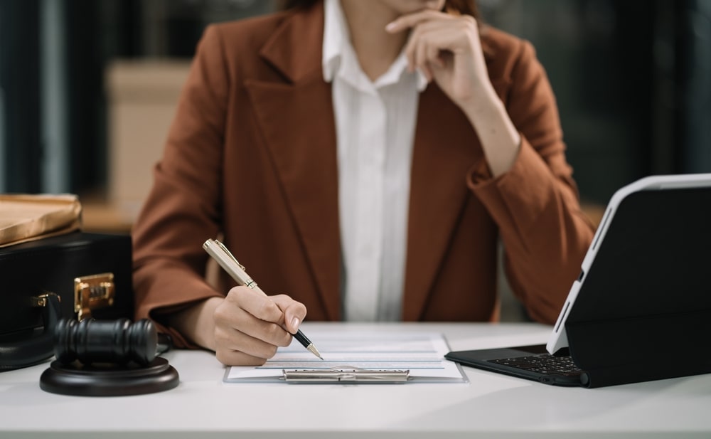 Professional woman at a desk reviewing legal documents with a gavel, pen, and laptop in front of her.