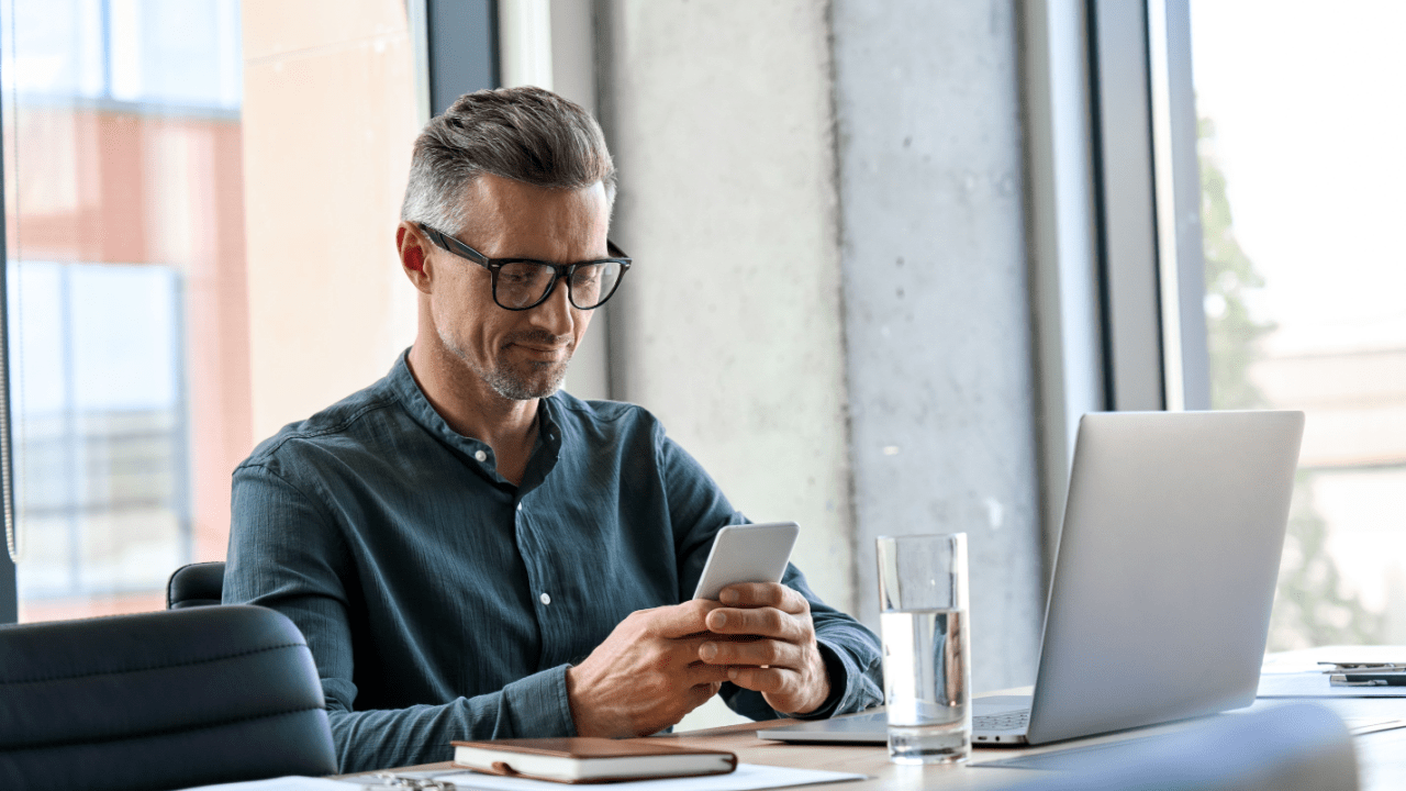 Professional man with glasses using smartphone and laptop to research average cost of traffic lawyer vs paying ticket, comparing legal fees and fines