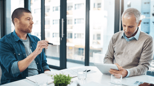 Two professional men consulting in modern office with documents and tablet, discussing legal outcomes with traffic lawyers and reviewing case strategies