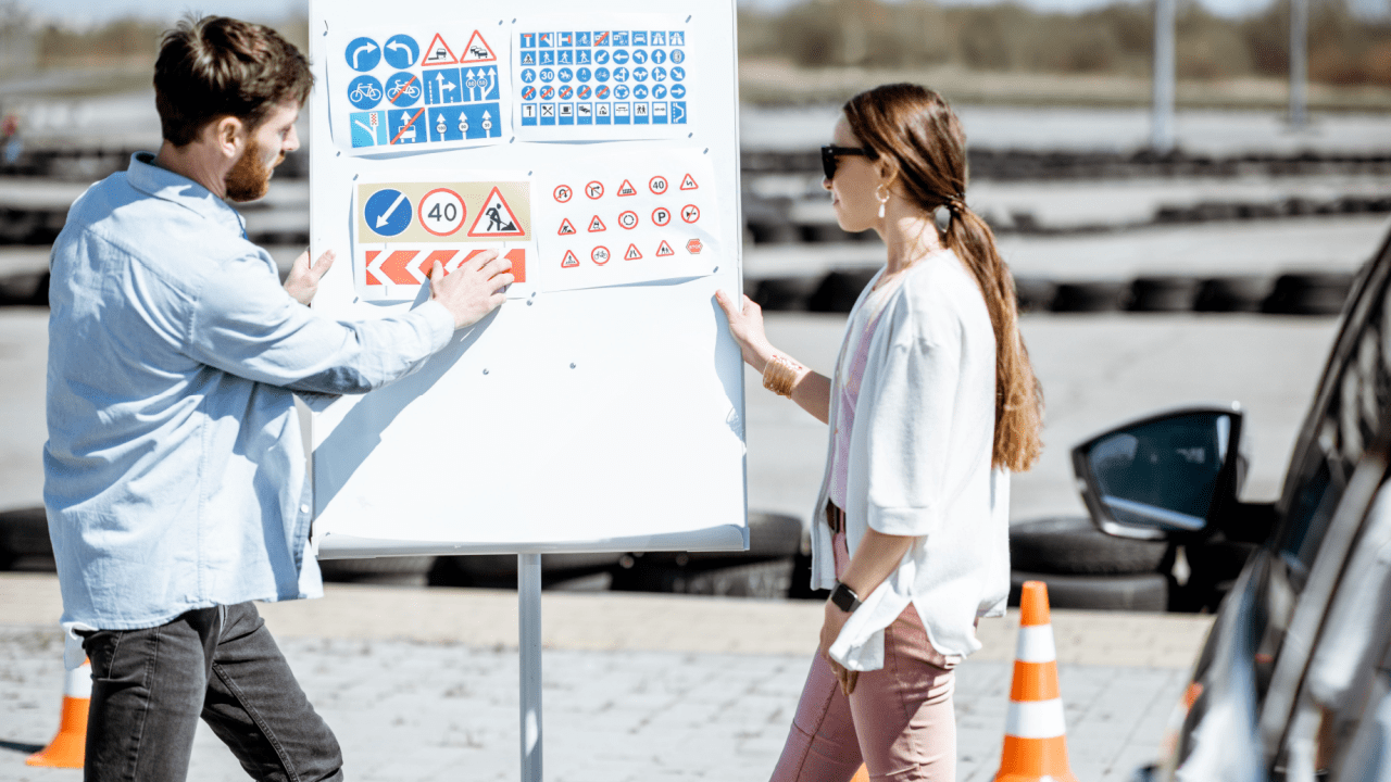 Two people learning what is the most important traffic rule of all by reviewing traffic signs and road safety symbols on educational board