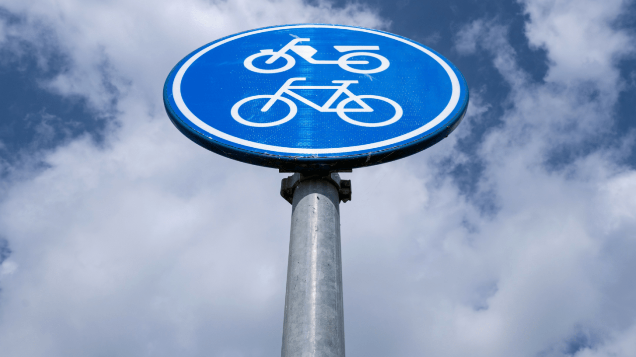 Blue traffic sign showing traffic laws for cyclists and bicycles on shared pathway against sky