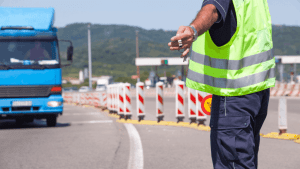Police officer conducting commercial vehicle traffic stop inspection at highway checkpoint with blue truck