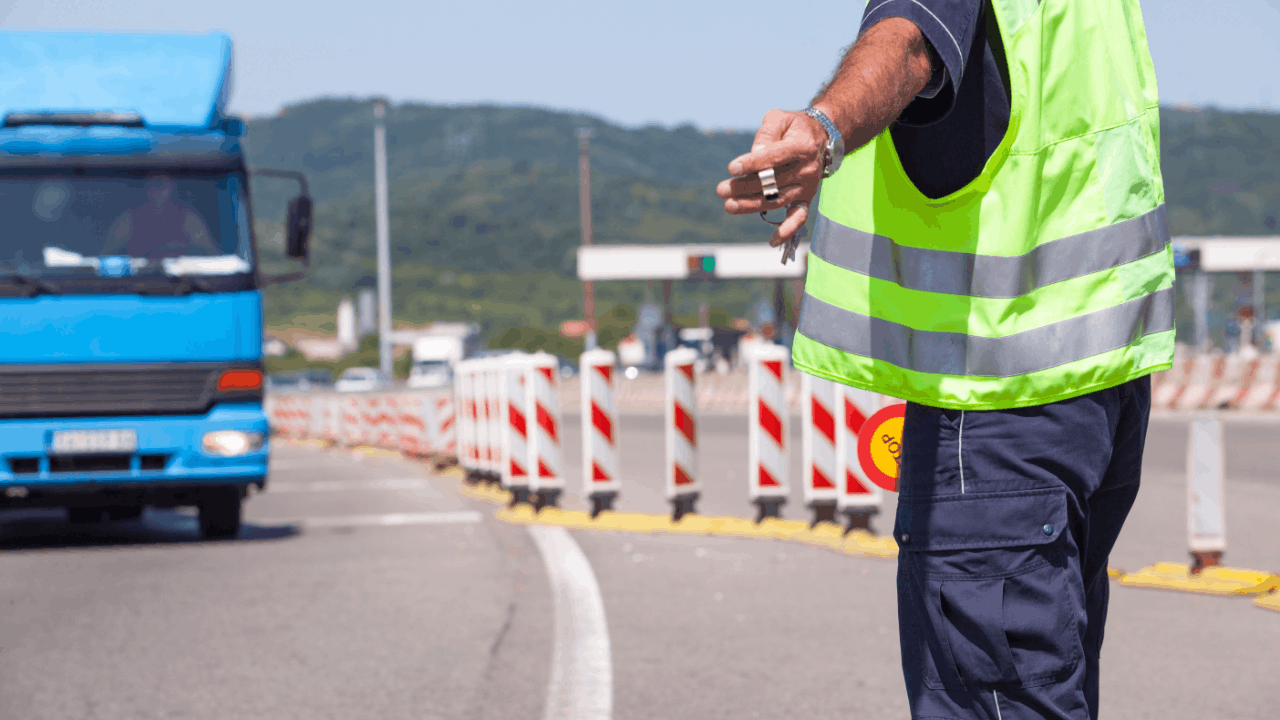 Police officer conducting commercial vehicle traffic stop inspection at highway checkpoint with blue truck