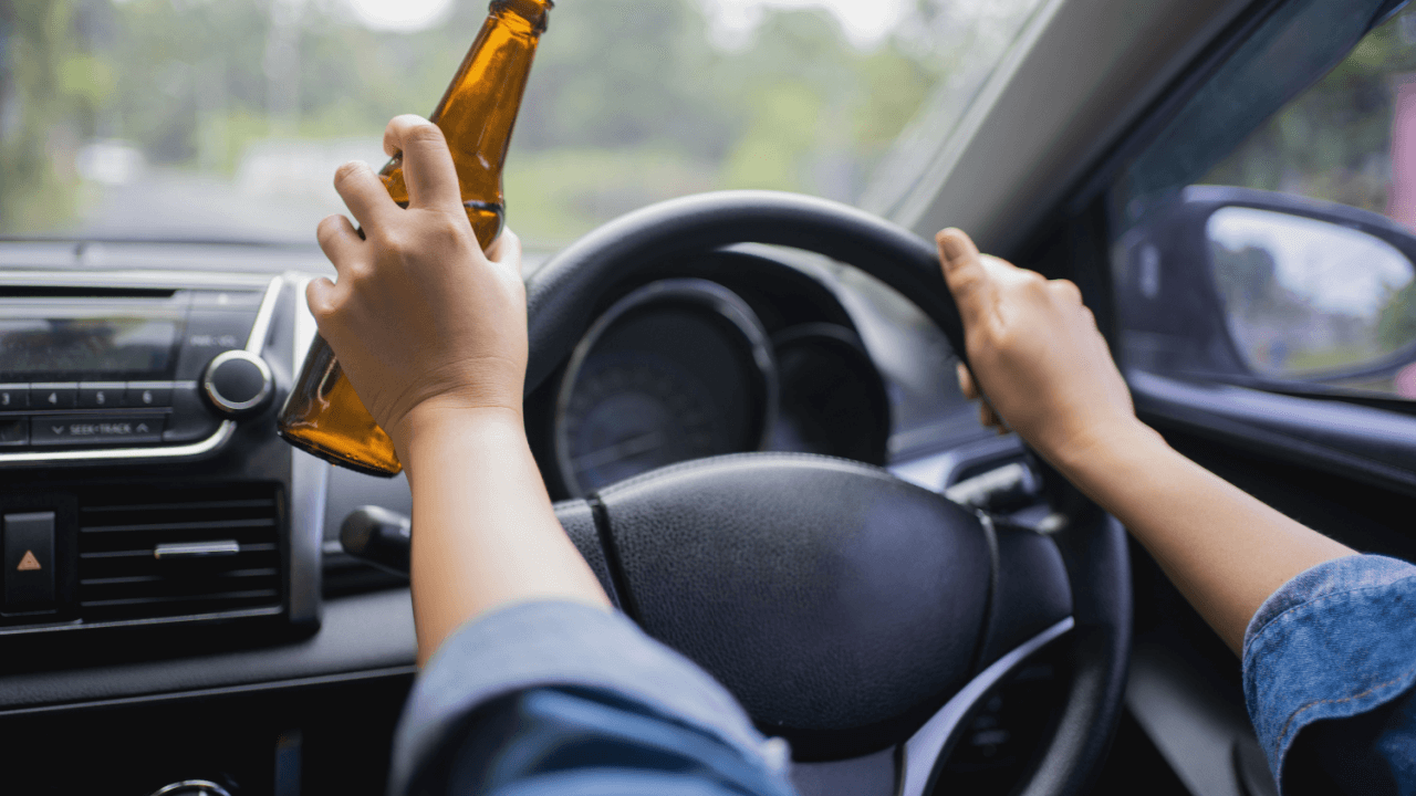 Is drunk driving illegal in all fifty states - driver holding alcohol bottle behind wheel risking DUI charges
