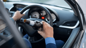Is it illegal to drink and drive in every state? Driver holding beer bottle behind wheel demonstrates illegal DUI behavior