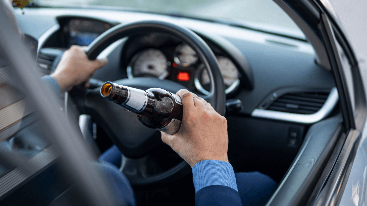 Is it illegal to drink and drive in every state? Driver holding beer bottle behind wheel demonstrates illegal DUI behavior