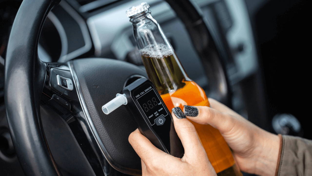Person holding breathalyzer and alcohol bottle in car illustrating what states have DUI laws
