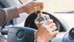 When was drunk driving made illegal in all states - person holding alcohol bottle behind steering wheel demonstrating DUI violation