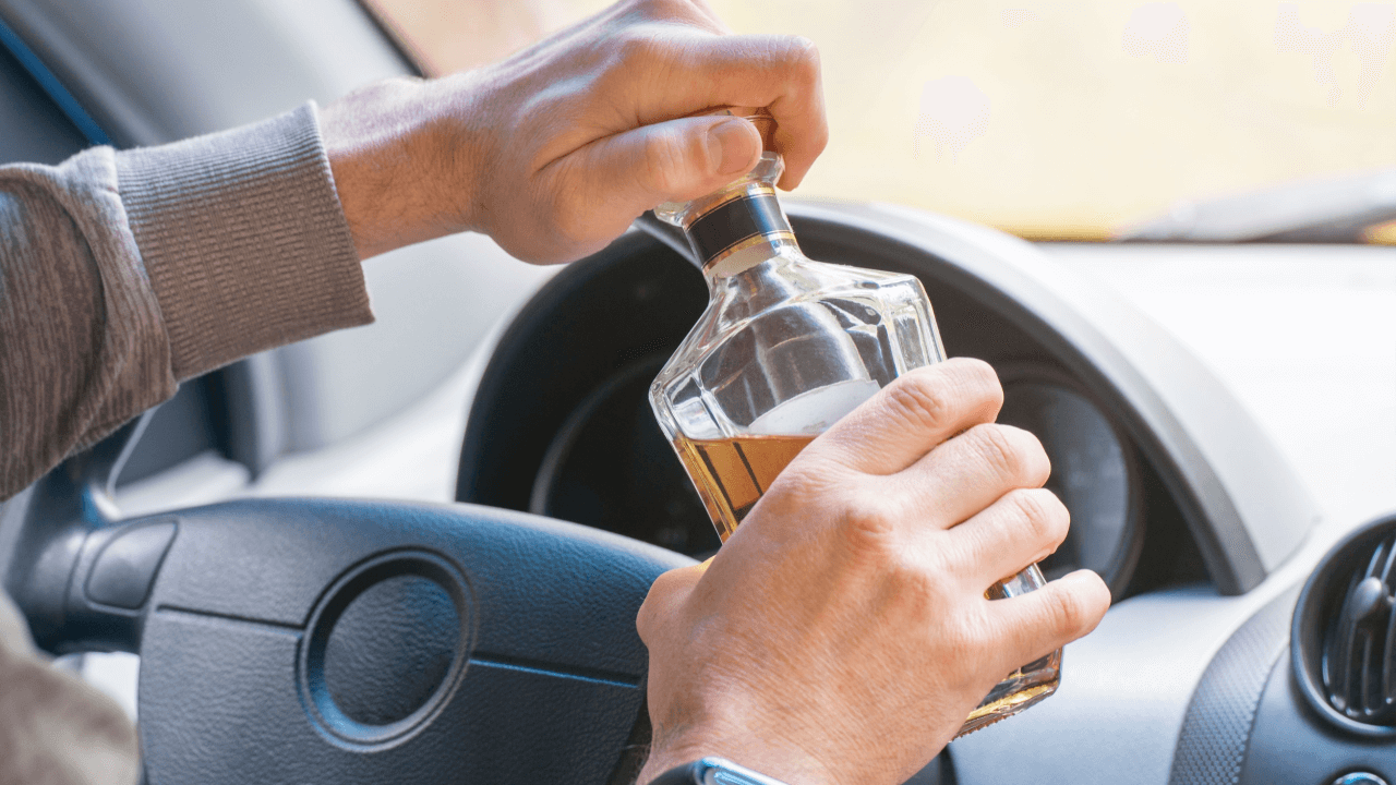 When was drunk driving made illegal in all states - person holding alcohol bottle behind steering wheel demonstrating DUI violation