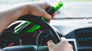 Person holding beer bottle behind steering wheel illustrating which state has the strictest laws for drunk driving