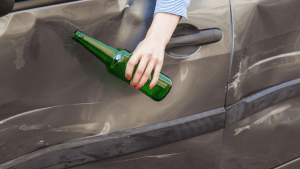 Person holding alcohol bottle near vehicle illustrating how many drinks equal the legal limit under state DUI laws