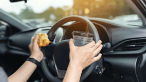 Driver holding food and drink while steering, illustrating what careless driving means behind the wheel
