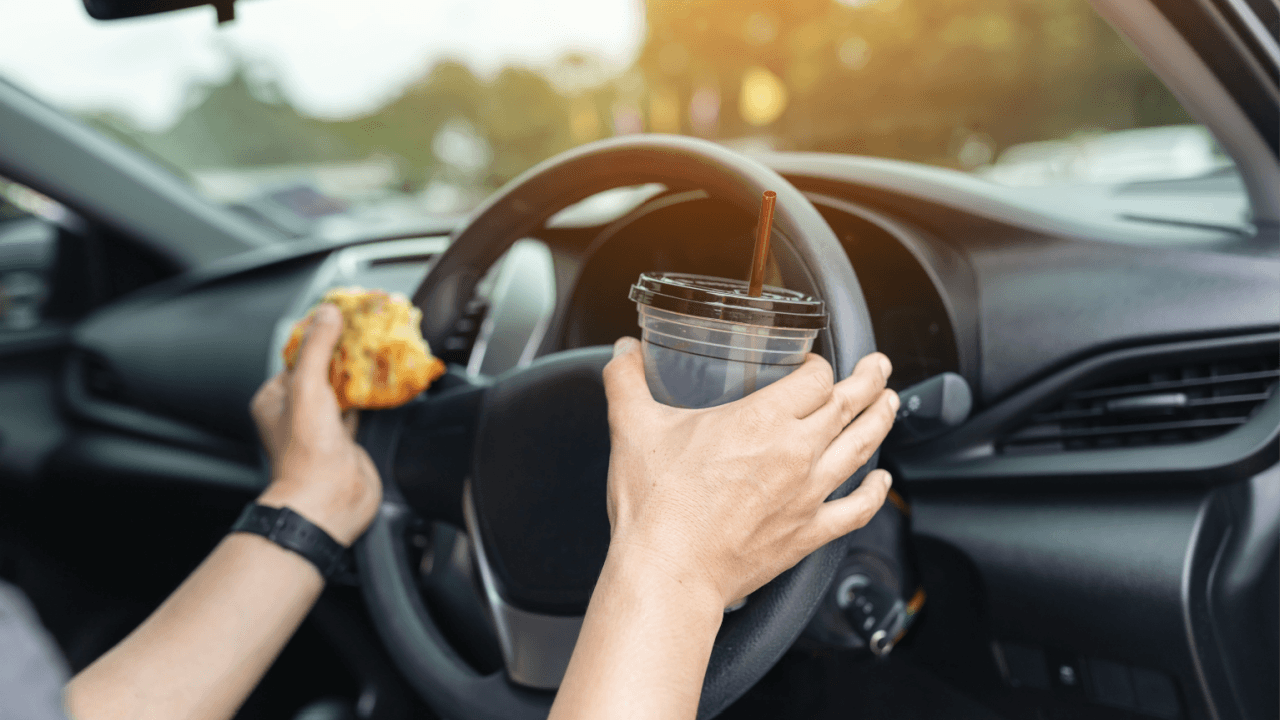 Driver holding food and drink while steering, illustrating what careless driving means behind the wheel