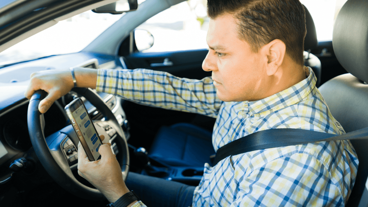 Man looking at smartphone while driving, illustrating what is considered careless driving under traffic law