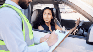 A woman driver looking stressed while a traffic officer writes a careless driving ticket beside her car window