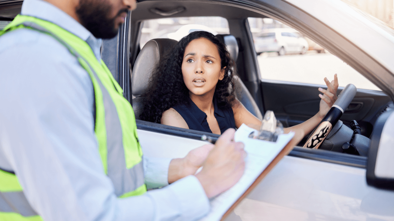 A woman driver looking stressed while a traffic officer writes a careless driving ticket beside her car window